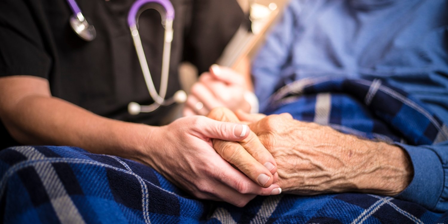 Close-up of caregiver holding hands with elderly patient.